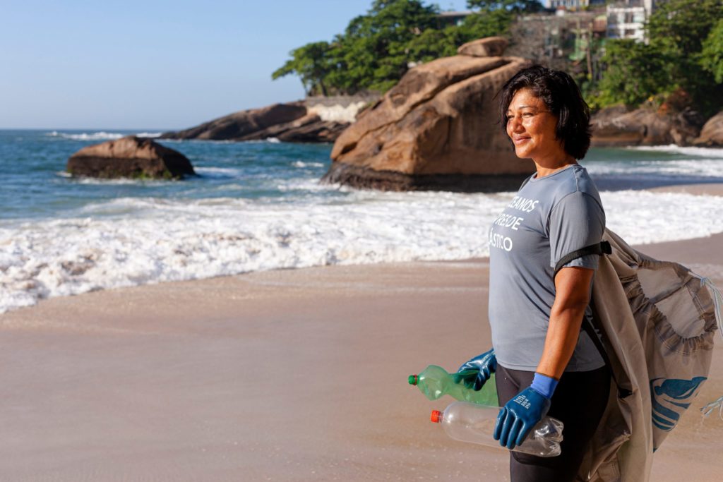 Plastic Bank female community member collecting plastic waste in front of the ocean in Brazil
