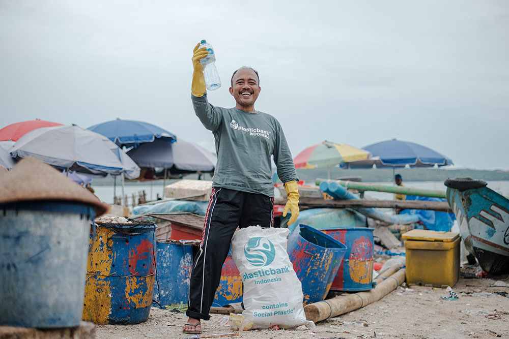 Plastic Bank male community member collecting plastic waste in front of the ocean in Kedonganan Beach, Bali