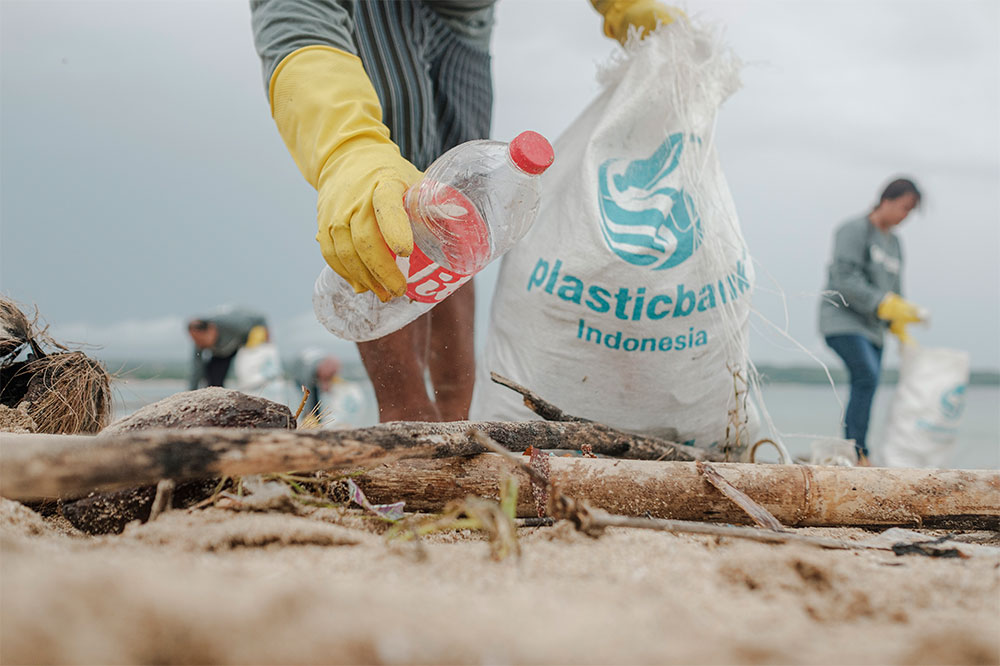 Plastic Bank male community member collecting plastic bottle in front of the ocean in Kedonganan Beach, Bali